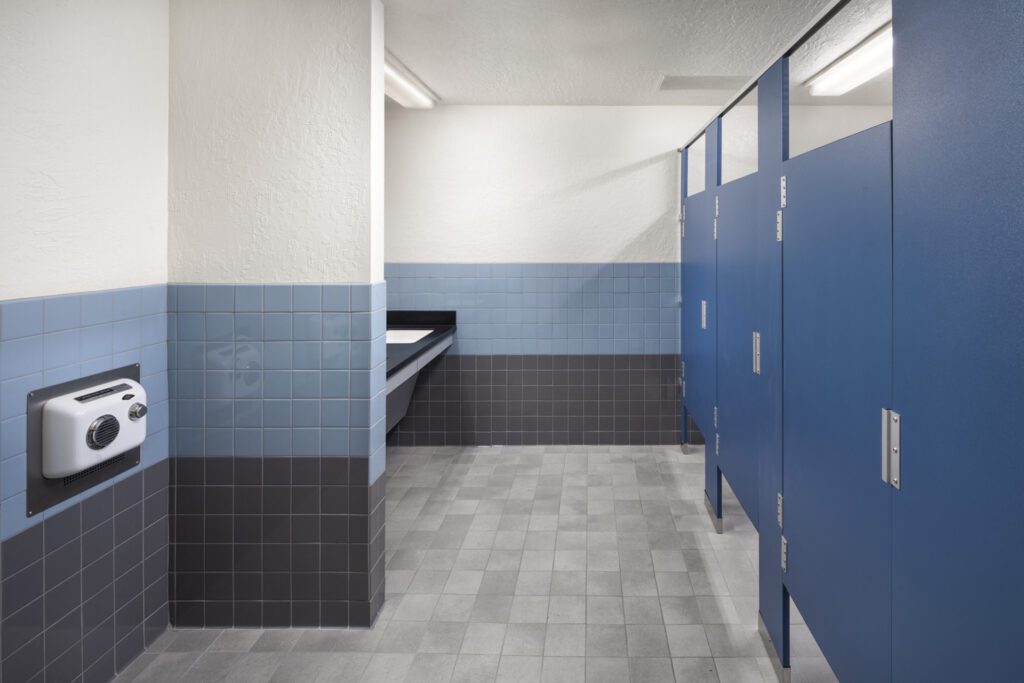 Public restroom interior, renovated for Alhambra Preschool Academy, with blue stall doors and tiled walls.