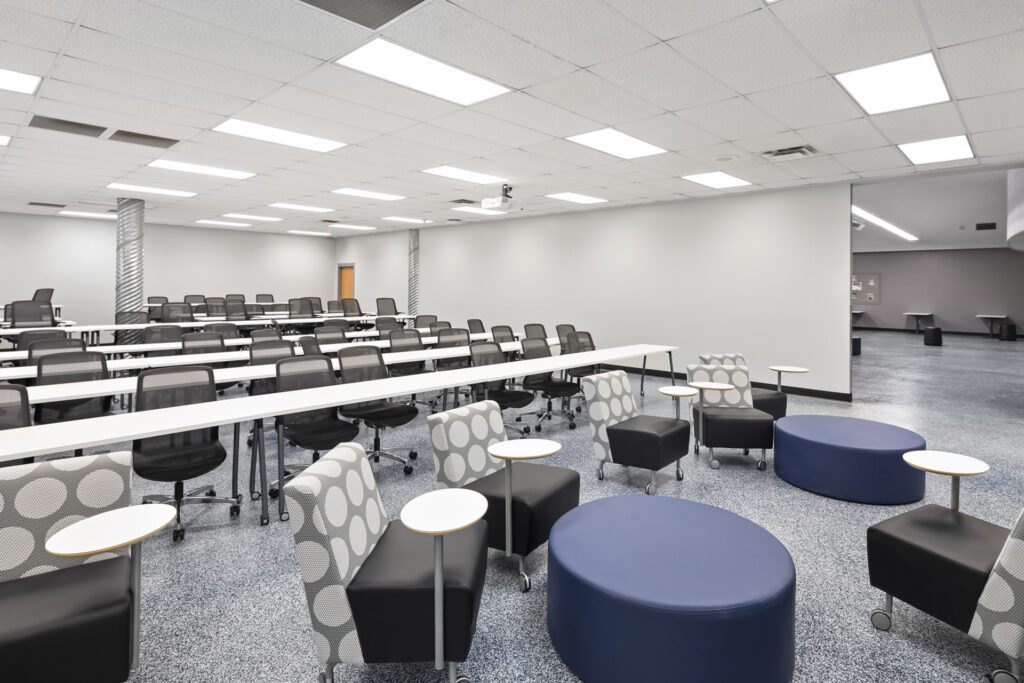 Modern classroom with rows of desks and chairs at Higley High School, featuring a casual seating area with patterned armchairs and round stools.