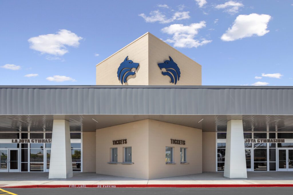 Modern school gymnasium entrance at La Joya High School with ticket booths and distinctive blue logo emblems.