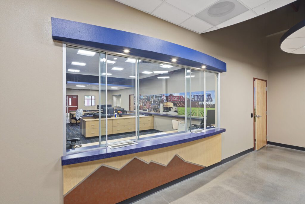 Office interior viewed from a lobby through a large window with a service counter, featuring Sierra Linda High School's Lobby Security Upgrades.