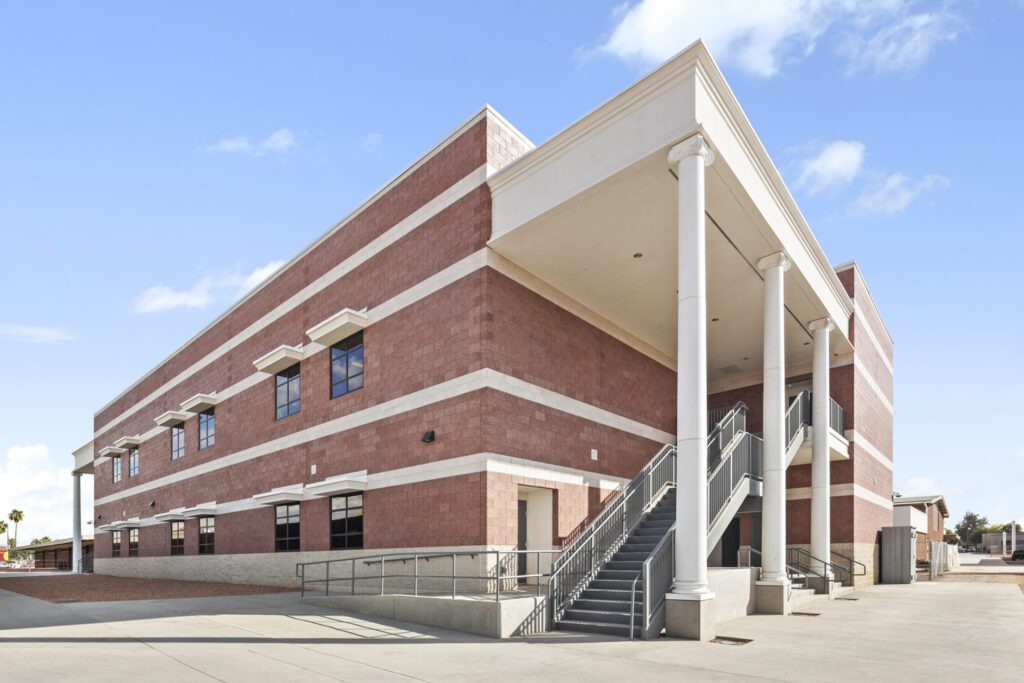 Modern two-story brick Science Building Addition with a columned entrance and exterior stairway under a clear sky at Tolleson Union High School.