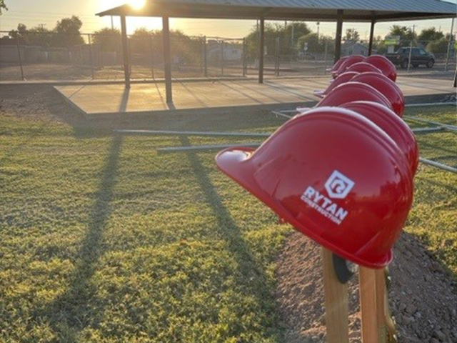 Line of red helmets on wooden posts at a home construction site with early morning light casting shadows on the grass.