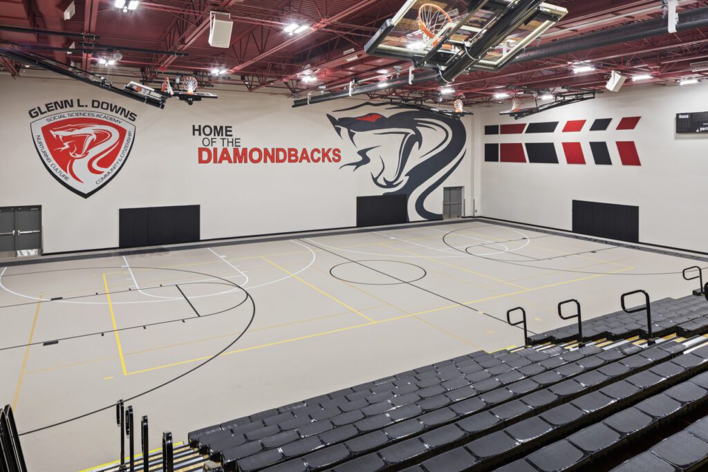 Indoor basketball court at the new gymnasium of Glenn L. Downs Social Sciences Academy with logo and mascot on the wall.