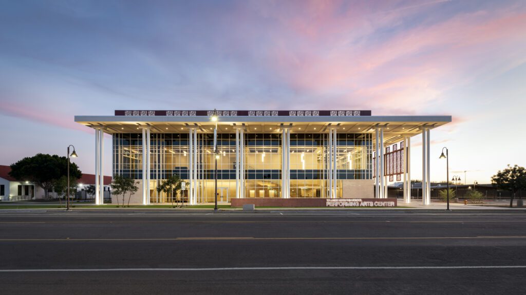 Modern glass-fronted building at the Tolleson Union High School Performing Arts Center at twilight with a colorful sky.