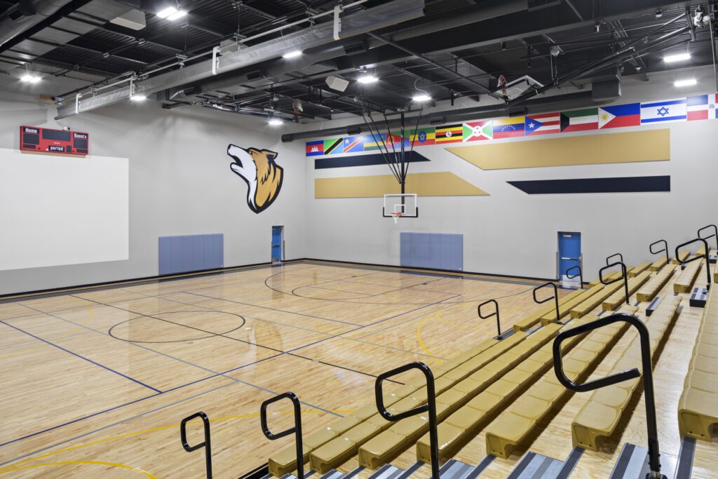 An empty modern gymnasium with basketball court, bleachers, and international flags on the wall at Global Academy of Phoenix.