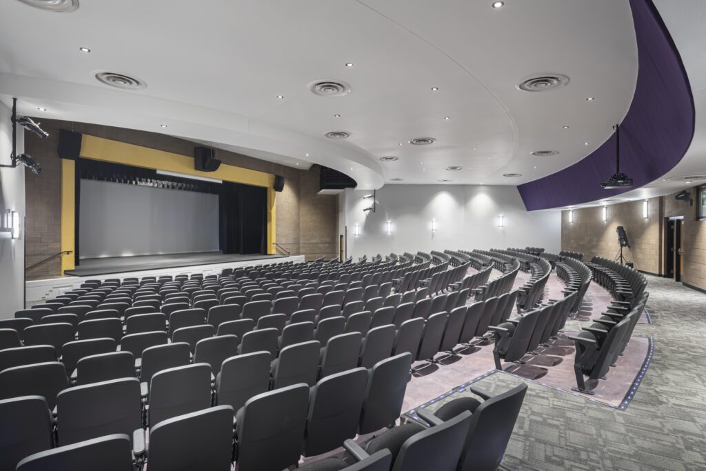 Modern auditorium at Cesar Chavez High School with rows of seating and a stage with a closed curtain.